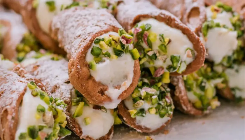 Słodkie rurki wypełnione kremowym serek ricotta, posypane cukrem pudrem i pistacjami. Pyszna włoska przekąska.