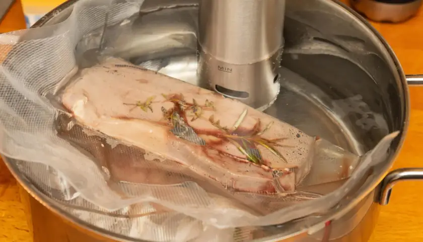 Mięso w woreczku z ziołami, zanurzone w wodzie z cyrkulatorem sous vide.