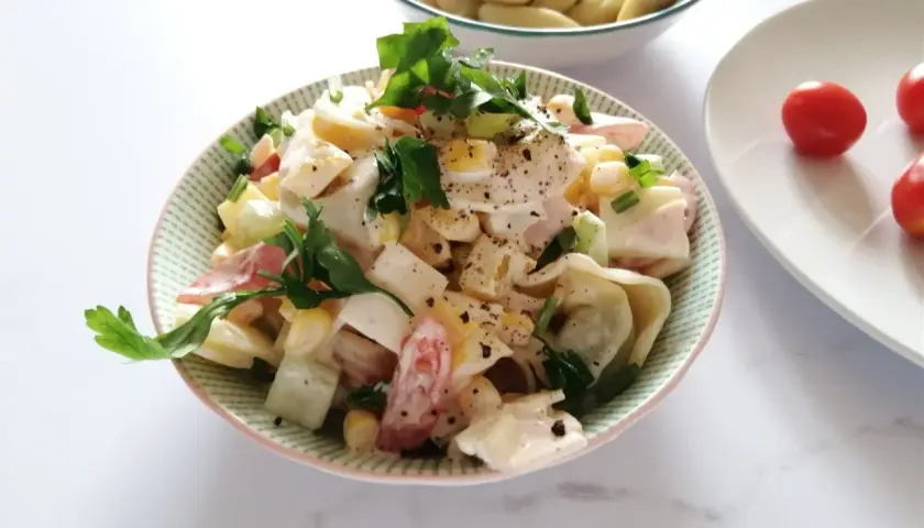 Pyszna sałatka z tortellini, jajka, kukurydzy i pomidorów, udekorowana natką pietruszki. Idealna na letnie dni, to najlepsza sałatka z tortellini.