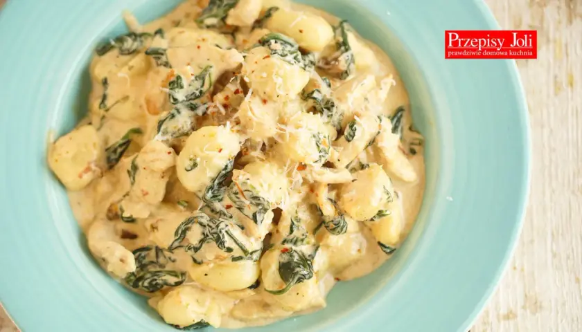 Pyszne gnocchi z kurczakiem i szpinakiem w kremowym sosie, posypane parmezanem. Danie wygląda apetycznie i zachęca do spróbowania.