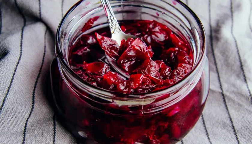 Słoik pełen aromatycznej konfitury z płatków róży, z łyżeczką zanurzoną w rubinowym, gęstym dżemie.