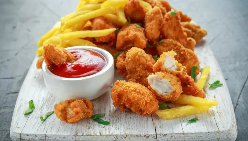 Chrupiące, złociste domowe nuggetsy jak z McDonalda, podane z frytkami i ketchupem na białej desce.