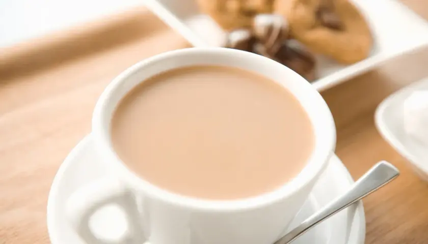 Aromaticzne cafe au lait w białej filiżance, obok ciasteczka z kawałkami czekolady. Idealny poranek.