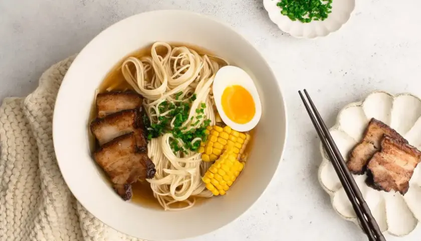 A miseczce aromatyczny shoyu ramen z makaronem, plastrami boczku, jajkiem na pół, kukurydzą i szczypiorkiem.