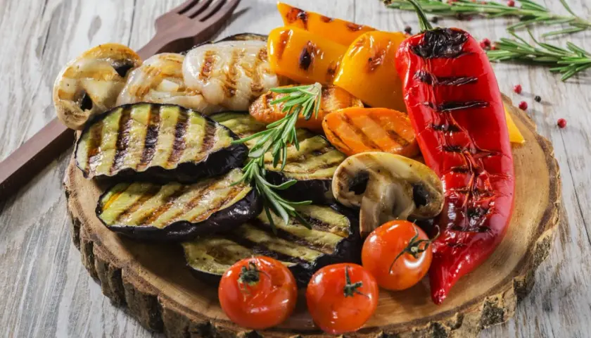 Co przygotować na grilla ze znajomymi? Grillowane bakłażany, papryki, pieczarki, pomidorki i marchewka na drewnianej desce.