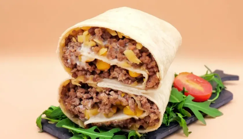 Pyszna tortilla z mięsem mielonym, kukurydzą i serem, przekrojona na pół, z rukolą i pomidorkiem.