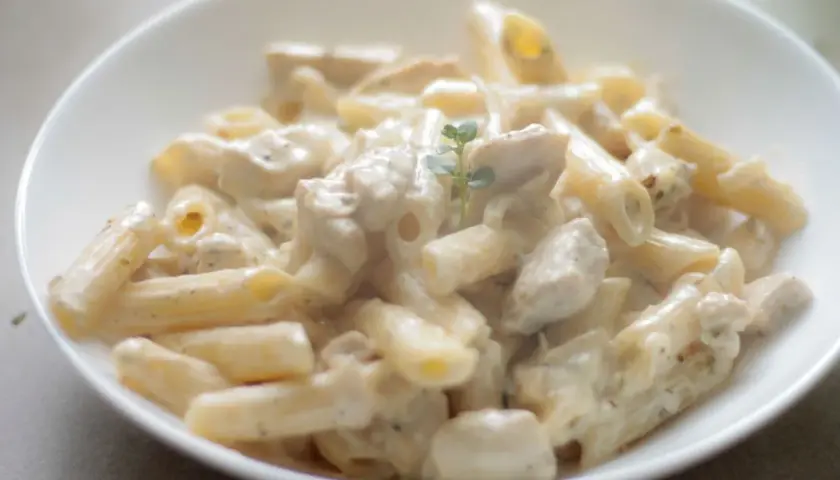 Penne z kurczakiem w kremowym sosie śmietanowym, udekorowane gałązką ziół. Pyszne danie gotowe do podania.