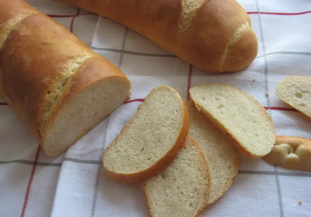 Chleb pszenny na zakwasie, pokrojony w kromki, leży na kratkowanym obrusie. Idealny do śniadania.