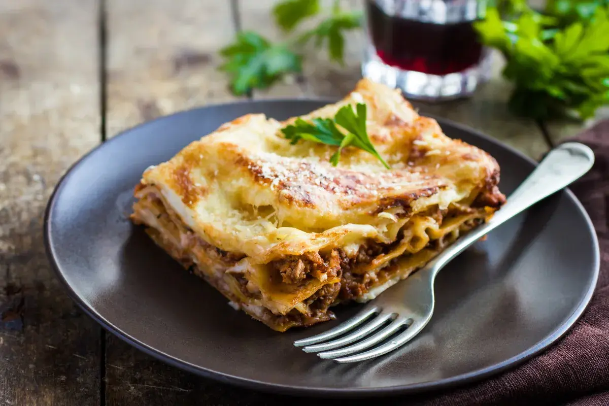 Pyszny kawałek lasagne z mięsem mielonym, idealny na prosty obiad. Posypana parmezanem i udekorowana natką pietruszki.