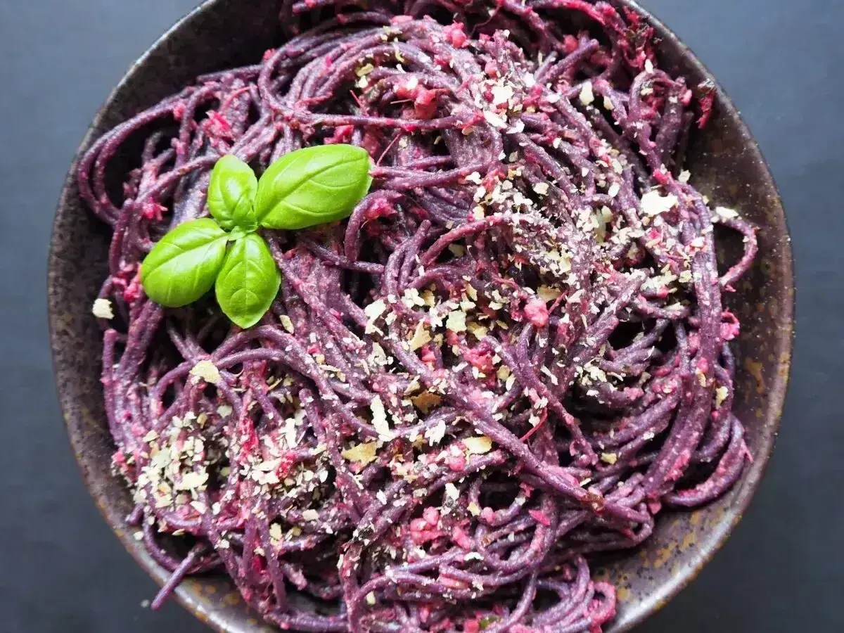 Fioletowy makaron z pesto ze słoika, posypany orzechami i udekorowany listkiem bazylii.