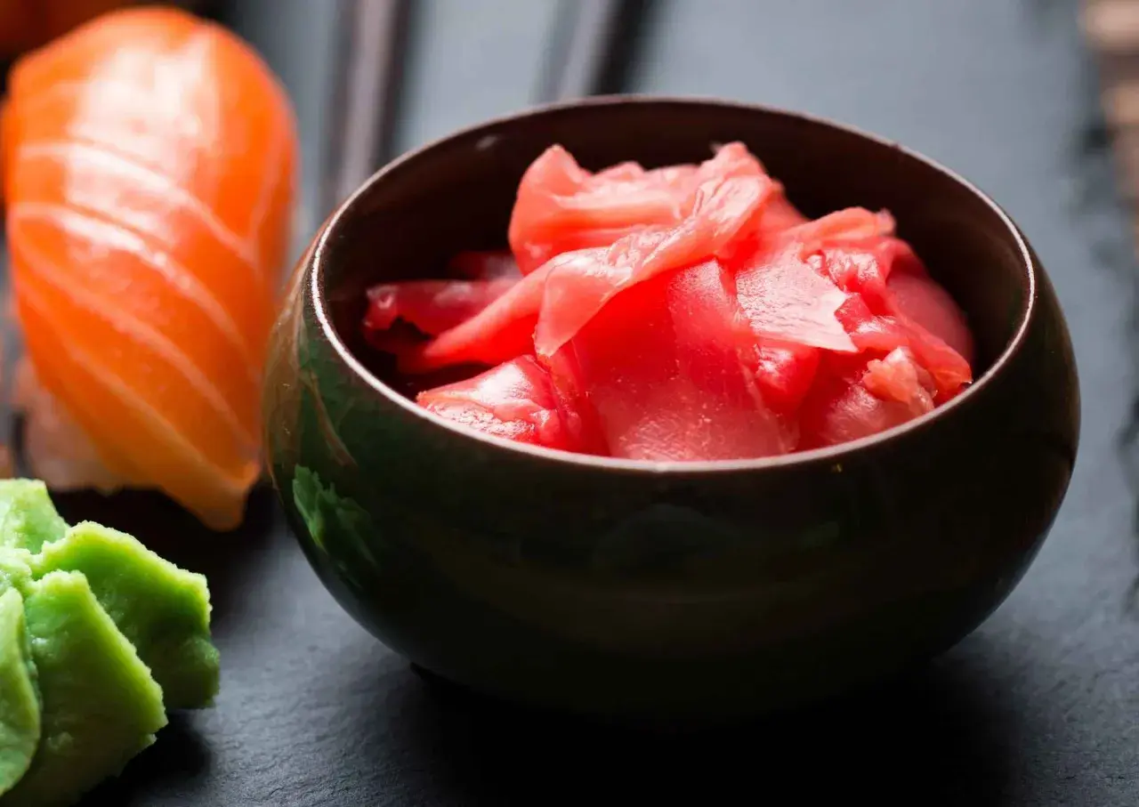 Miseczka z różowym, marynowanym imbirem obok sushi i wasabi. Idealny dodatek do japońskich smaków.