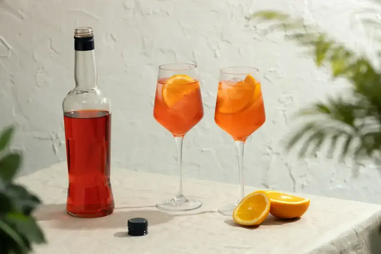Butelka Aperolu i dwa drinki z pomarańczą, idealne na lato. Poznaj prosty aperol przepis!