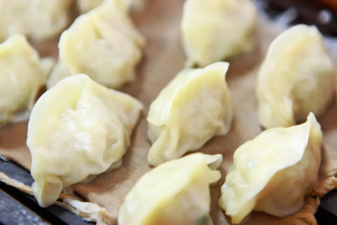 Parowane pierożki dim sum, delikatnie ułożone na brązowym papierze, kuszą swoim wyglądem.