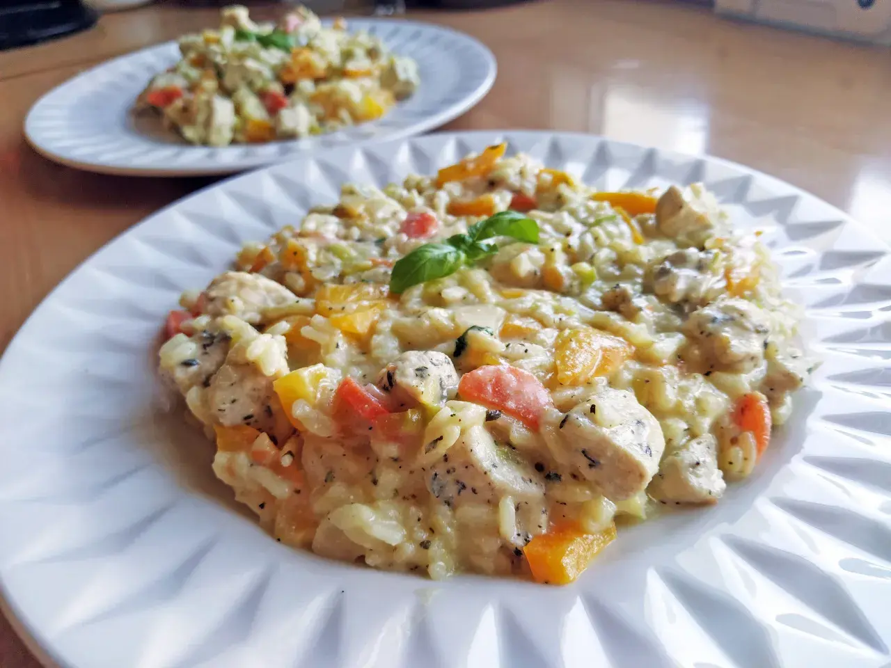 Szybkie risotto z warzywami i kurczakiem, udekorowane listkiem bazylii. Pyszne i kolorowe danie na talerzu.