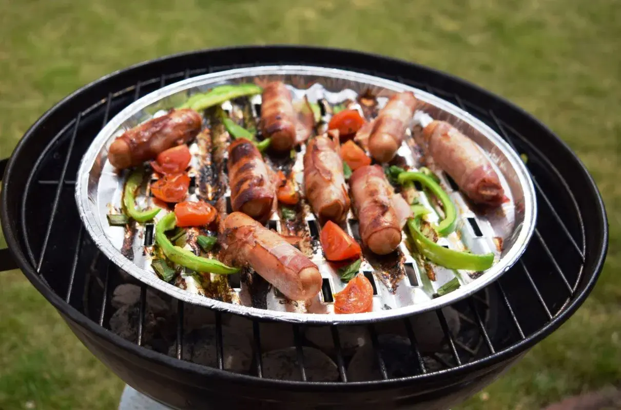 Pyszna kiełbasa z grilla, zawinięta w boczek, pieczona z papryką i pomidorkami na rozgrzanym ruszcie.