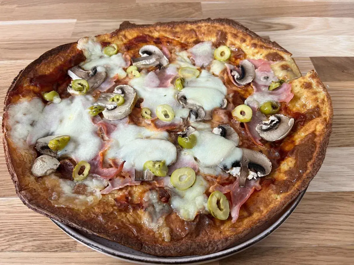 Pyszna pizza z twarogu z pieczarkami, szynką i oliwkami, zapieczona na złoto.