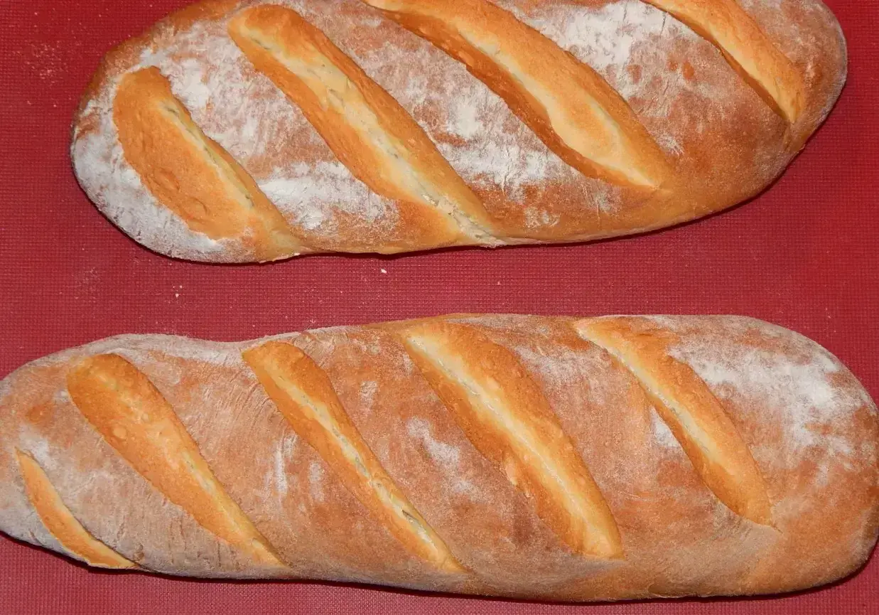 Dwie świeże bułki wrocławskie, lekko oprószone mąką, leżą na czerwonym tle.