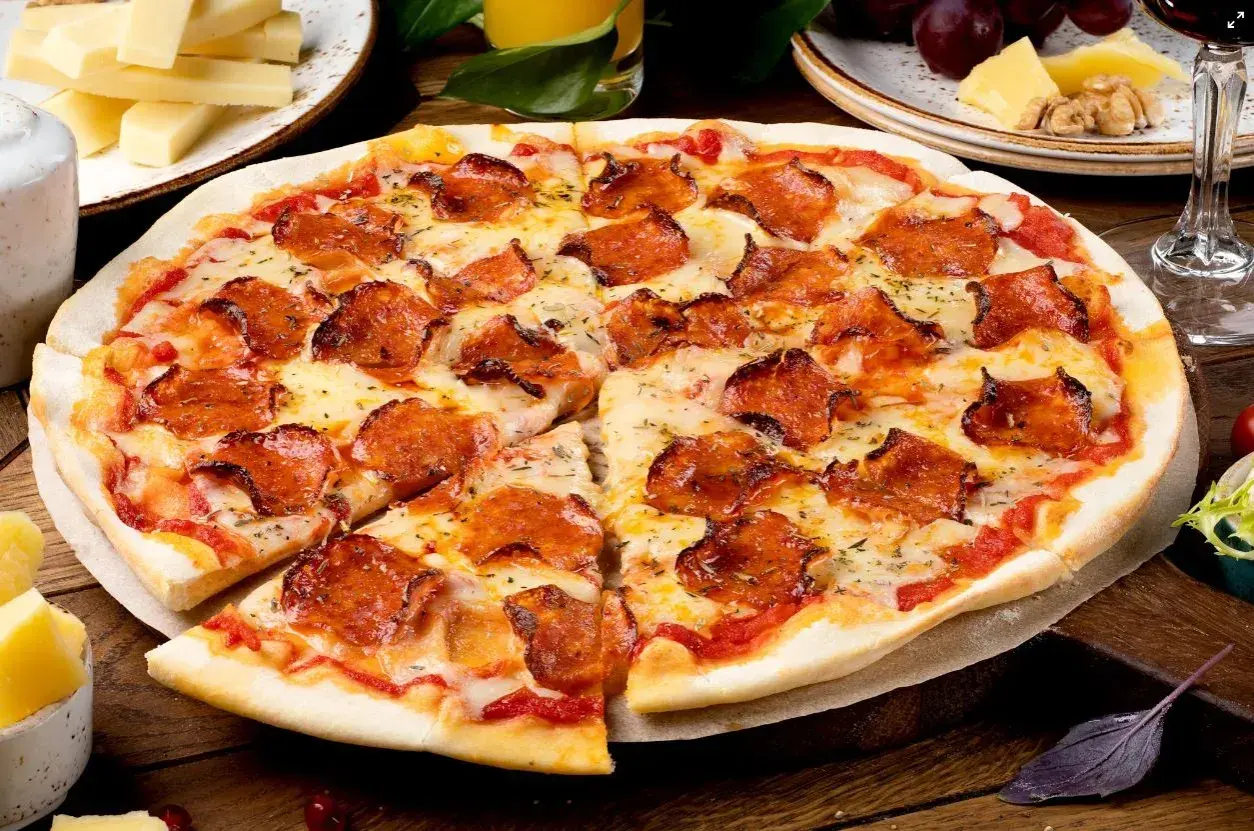 Pyszna pizza pepperoni z ciągnącym serem, obok serowe dodatki do pizzy, winogrona i kieliszek czerwonego wina.