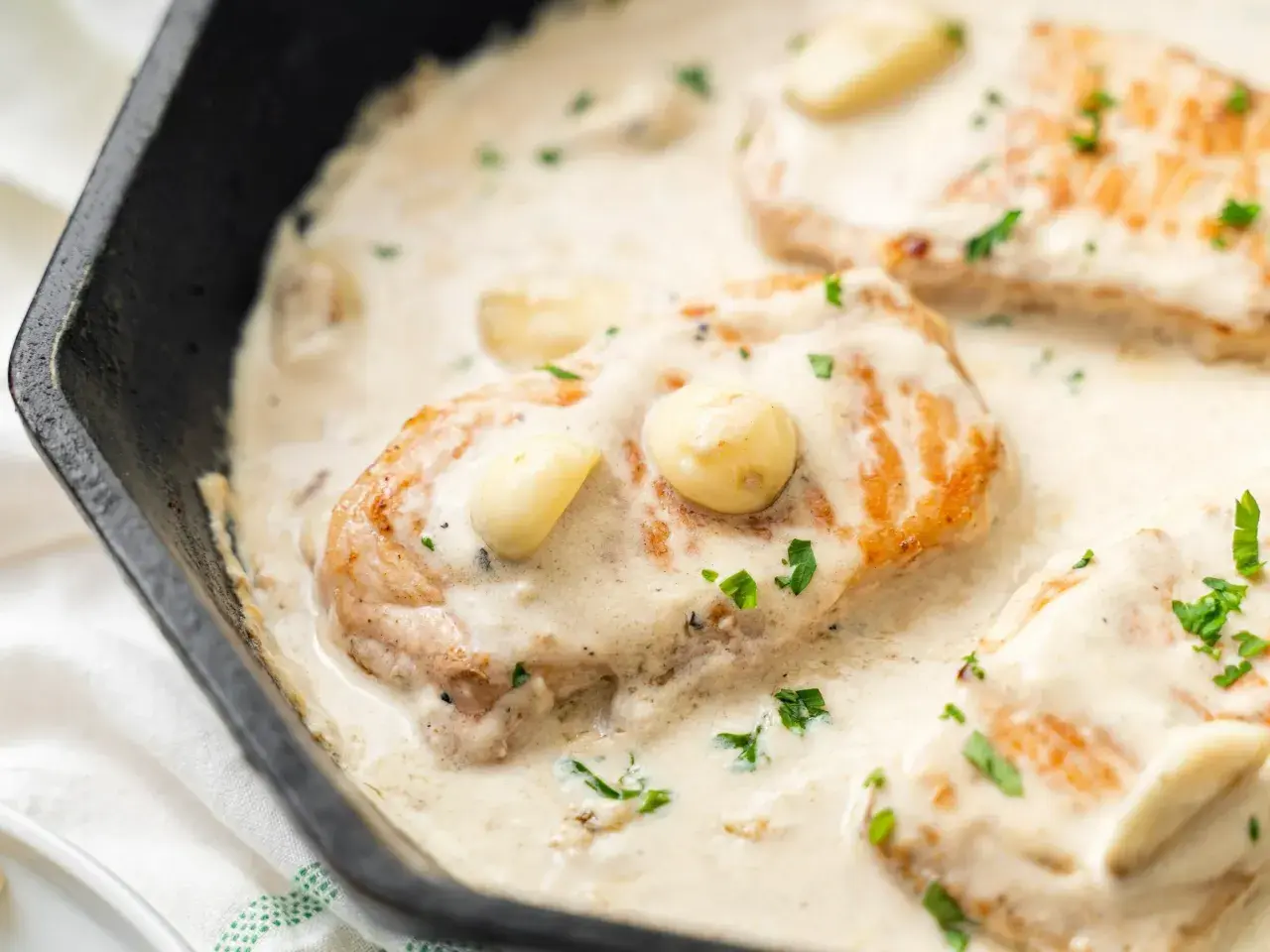 Smażony filet z kurczaka w kremowym sosie z czosnkiem i natką pietruszki, podany na patelni.