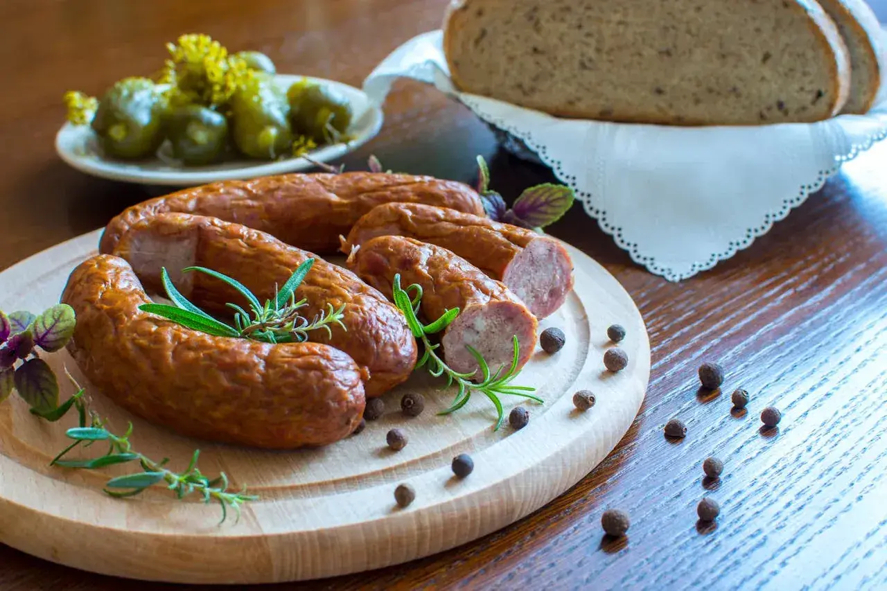Pyszna kiełbasa z piekarnika, podana z chlebem i ogórkami, ozdobiona rozmarynem i pieprzem.