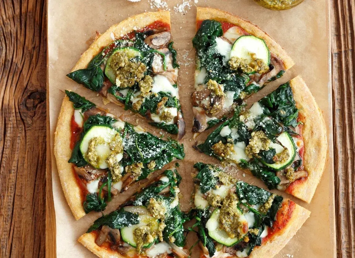 Pyszna pizza ze szpinakiem, cukinią i grzybami, polana sosem pesto.
