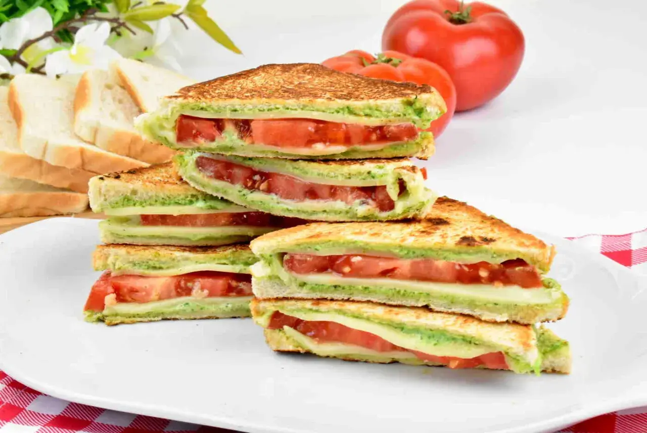 Pyszne włoskie kanapki z serem, pomidorami i zielonym pesto, ułożone na talerzu.