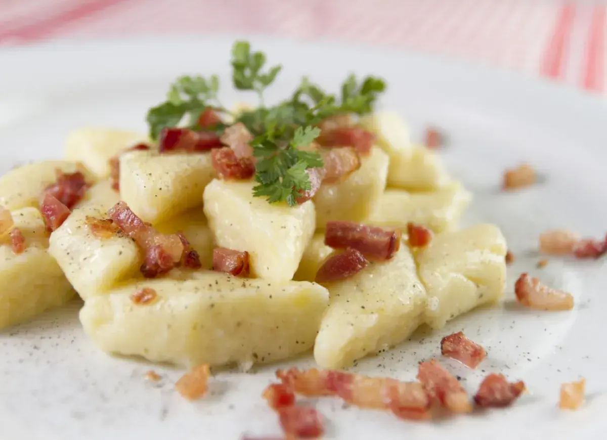 Kopytka z chrupiącym boczkiem i natką pietruszki, posypane pieprzem. Pyszne danie, które zadowoli każdego smakosza.