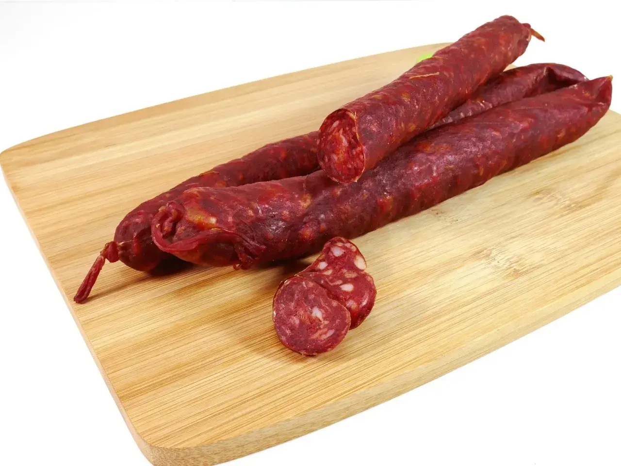 Trzy długie kiełbaski chorizo leżą na drewnianej desce. Jedna jest przekrojona, ukazując charakterystyczny, czerwony środek.