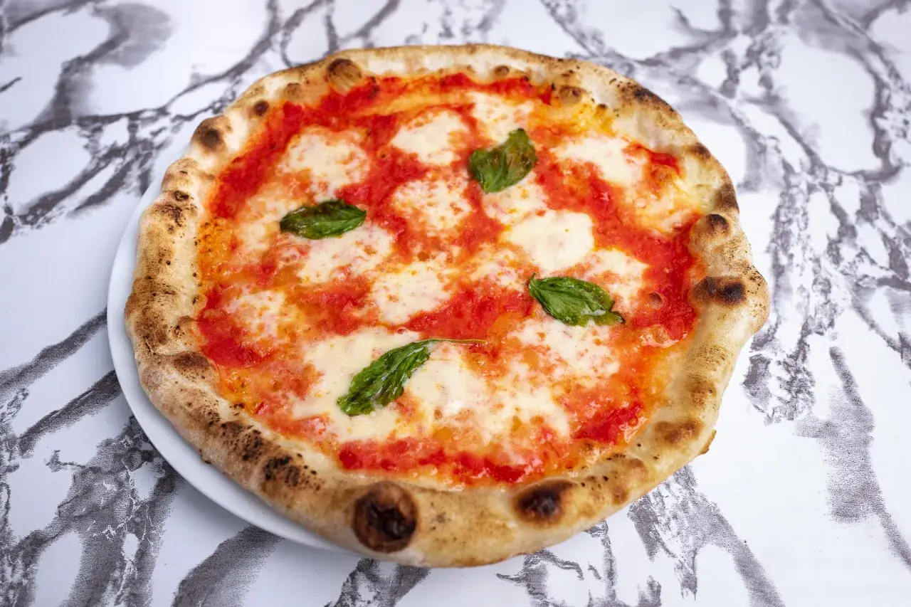 Pyszne ciasto na pizzę neapolitańską z pomidorami, mozzarellą i bazylią, idealne na letni wieczór.