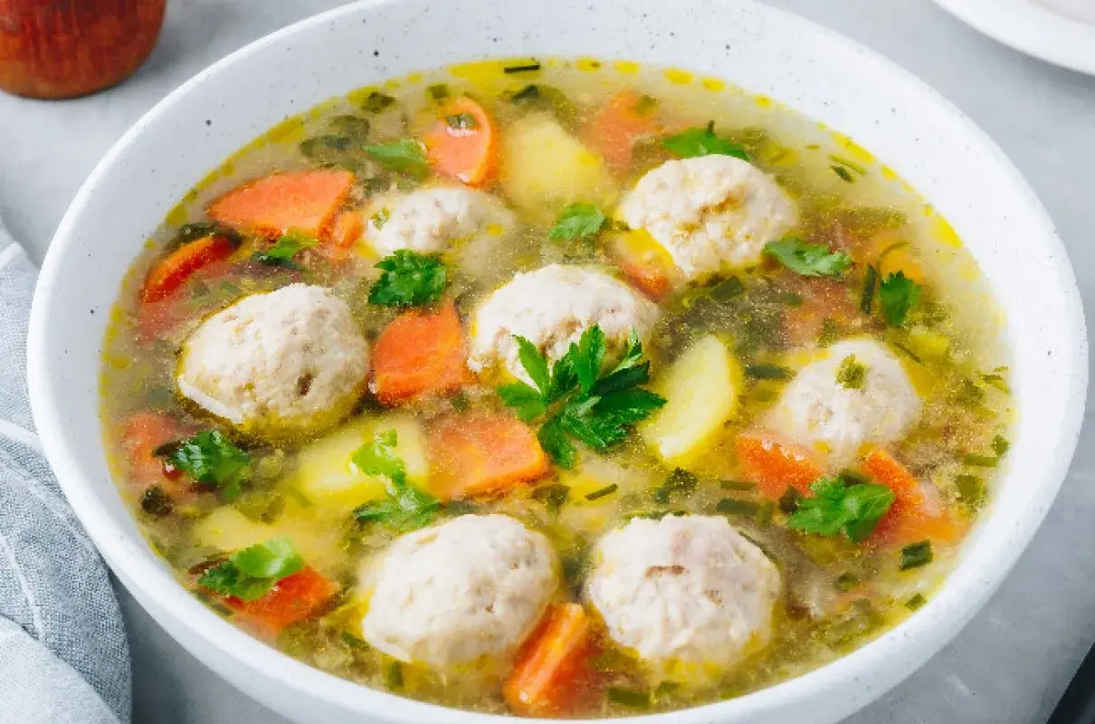 Zupa klopsowa babci: aromatyczny bulion z klopsikami, ziemniakami i marchewką, posypana natką pietruszki.