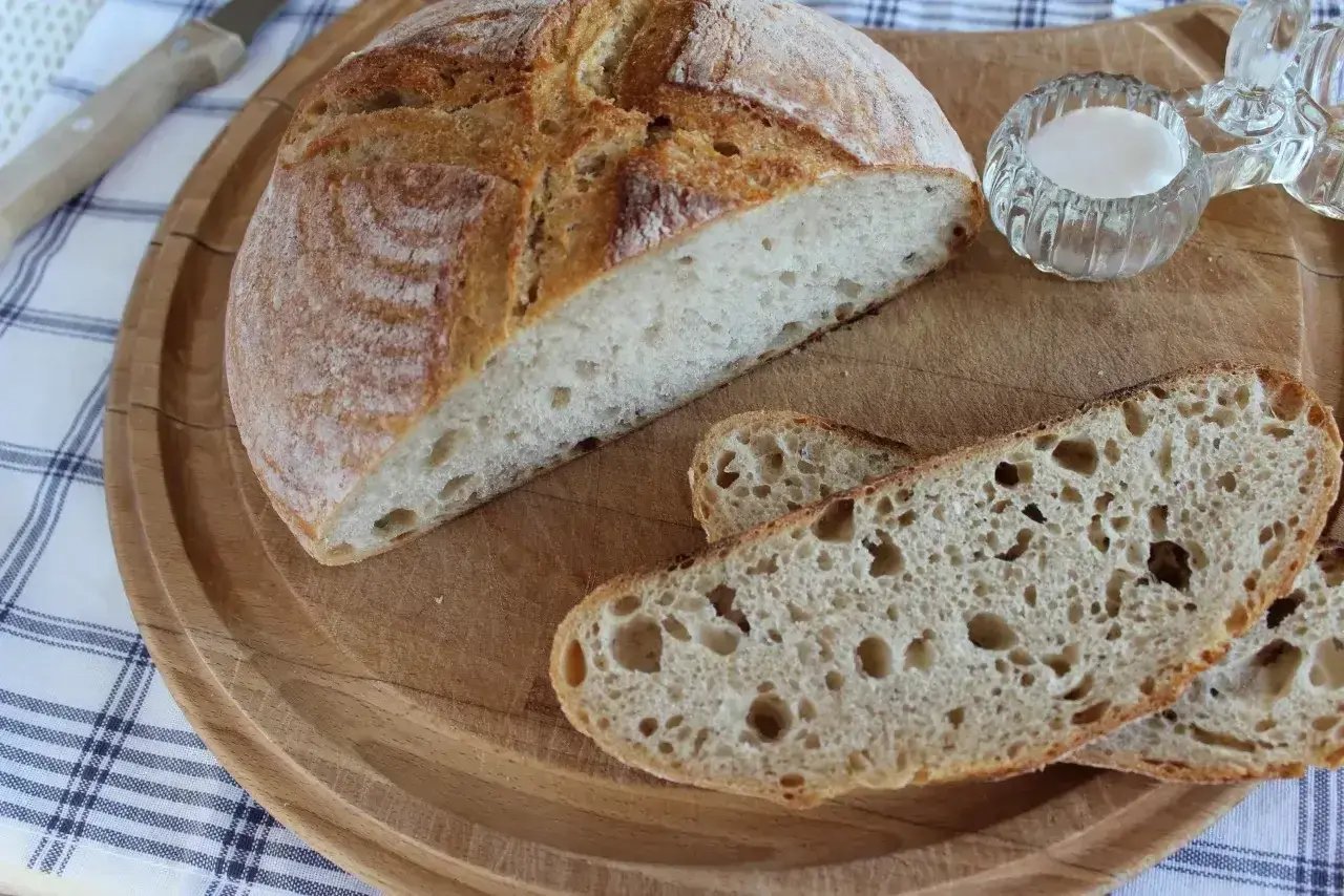 Chleb żytni na zakwasie, pokrojony na desce, z solniczką i nożem w tle. Idealny na śniadanie.