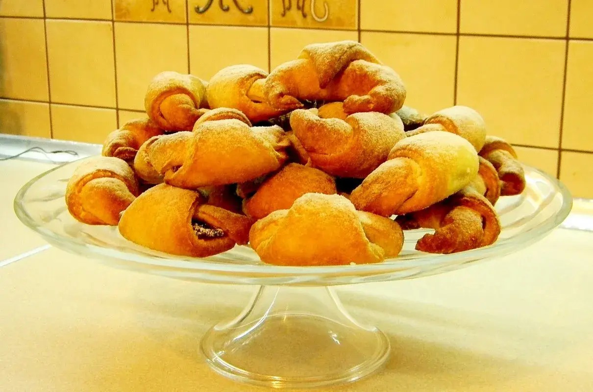 Stos rogalików drożdżowych, przygotowanych według przepisu babci, na szklanej paterze.