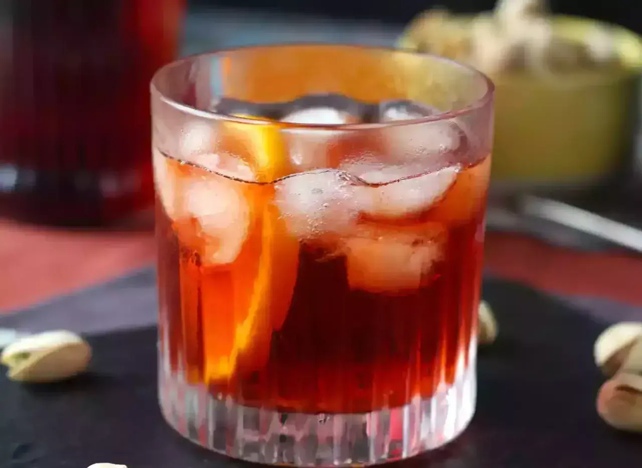 Klasyczny negroni przepis: czerwony koktajl z lodem i pomarańczą w szklance, obok pistacje.