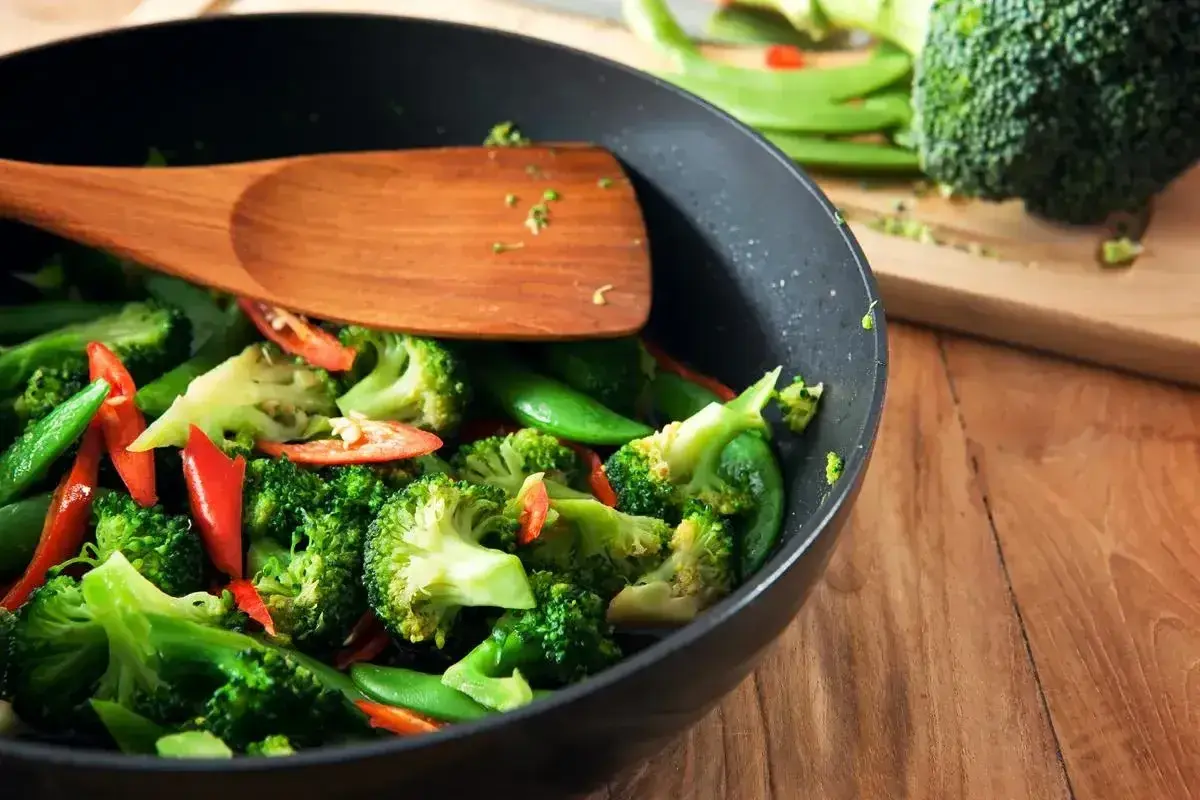 Brokuły, groszek cukrowy i papryczka chili w woku, gotowe do stir fry. Drewniana łopatka miesza warzywa.
