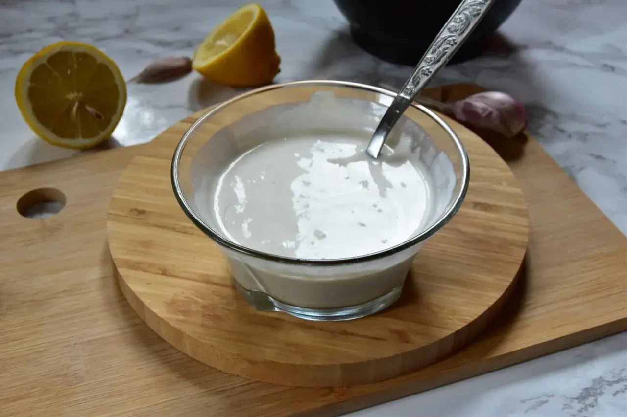 Kremowe aioli w miseczce, obok cytryna i czosnek. Idealne do dipów i sosów.