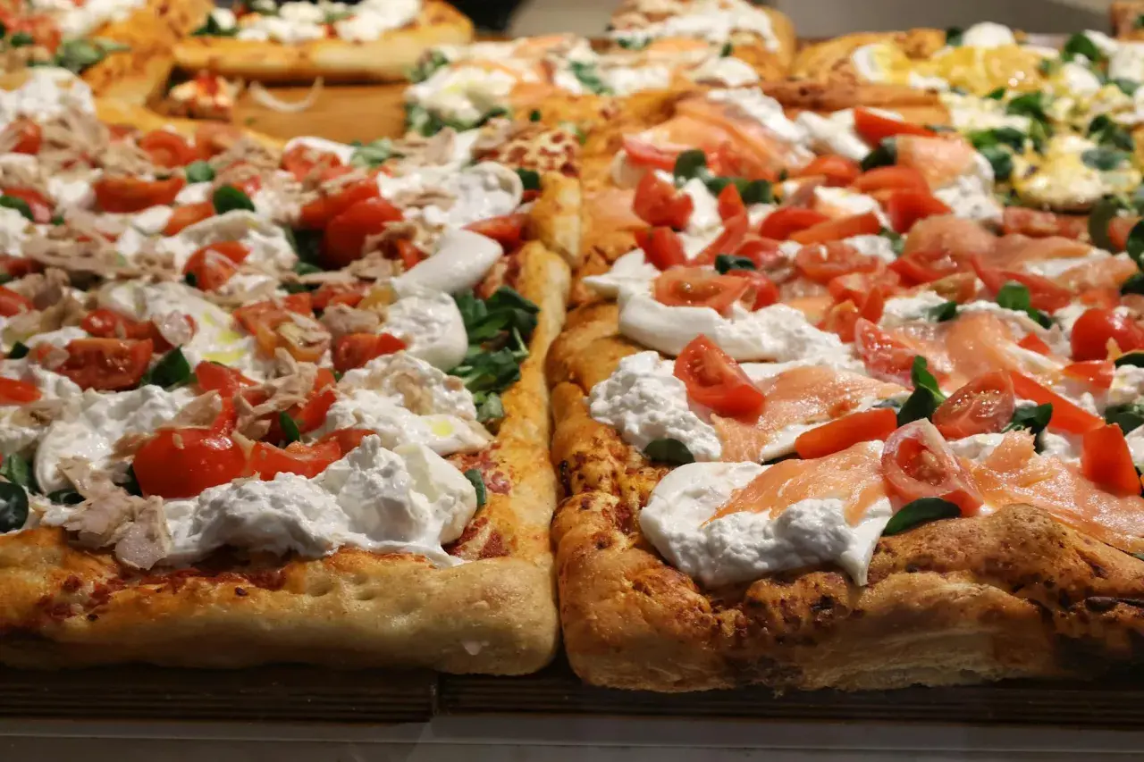 Dwie prostokątne pizze z burratą, pomidorkami i łososiem lub tuńczykiem. Puszyste ciasto, kremowy ser i świeże dodatki kuszą swoim wyglądem.