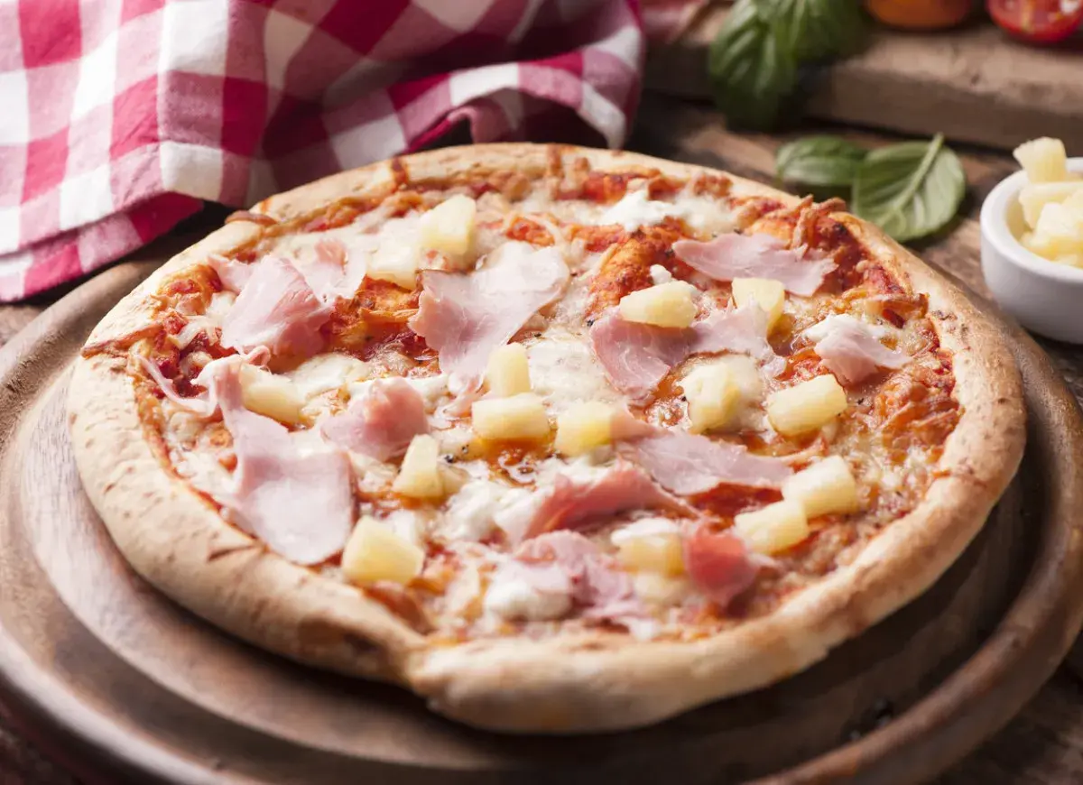 Apetyczna pizza z ananasem i szynką, polana ciągnącym się serem, na drewnianej desce.