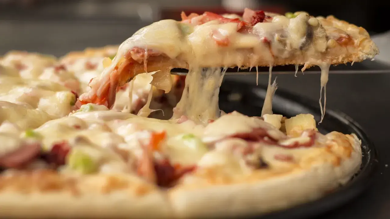 Gorąca, ciągnąca się pizza mrożona z serem, szynką i ananasem. Kawałek pizzy jest podnoszony, odsłaniając roztopiony ser.