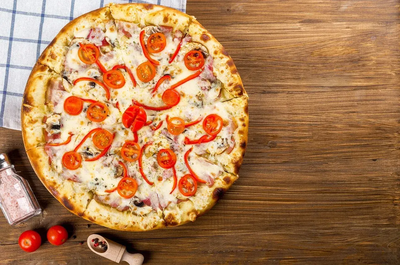 Apetyczna pizza capricciosa z pomidorkami, papryką i serem na drewnianym blacie.