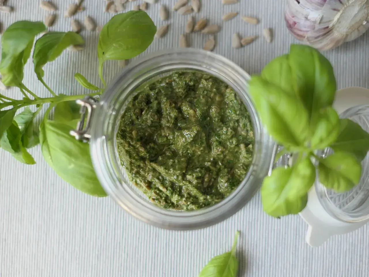 Domowe pesto z bazylii w słoiku, obok nasion słonecznika i czosnku. Idealne, by dowiedzieć się, jak zrobić pesto.