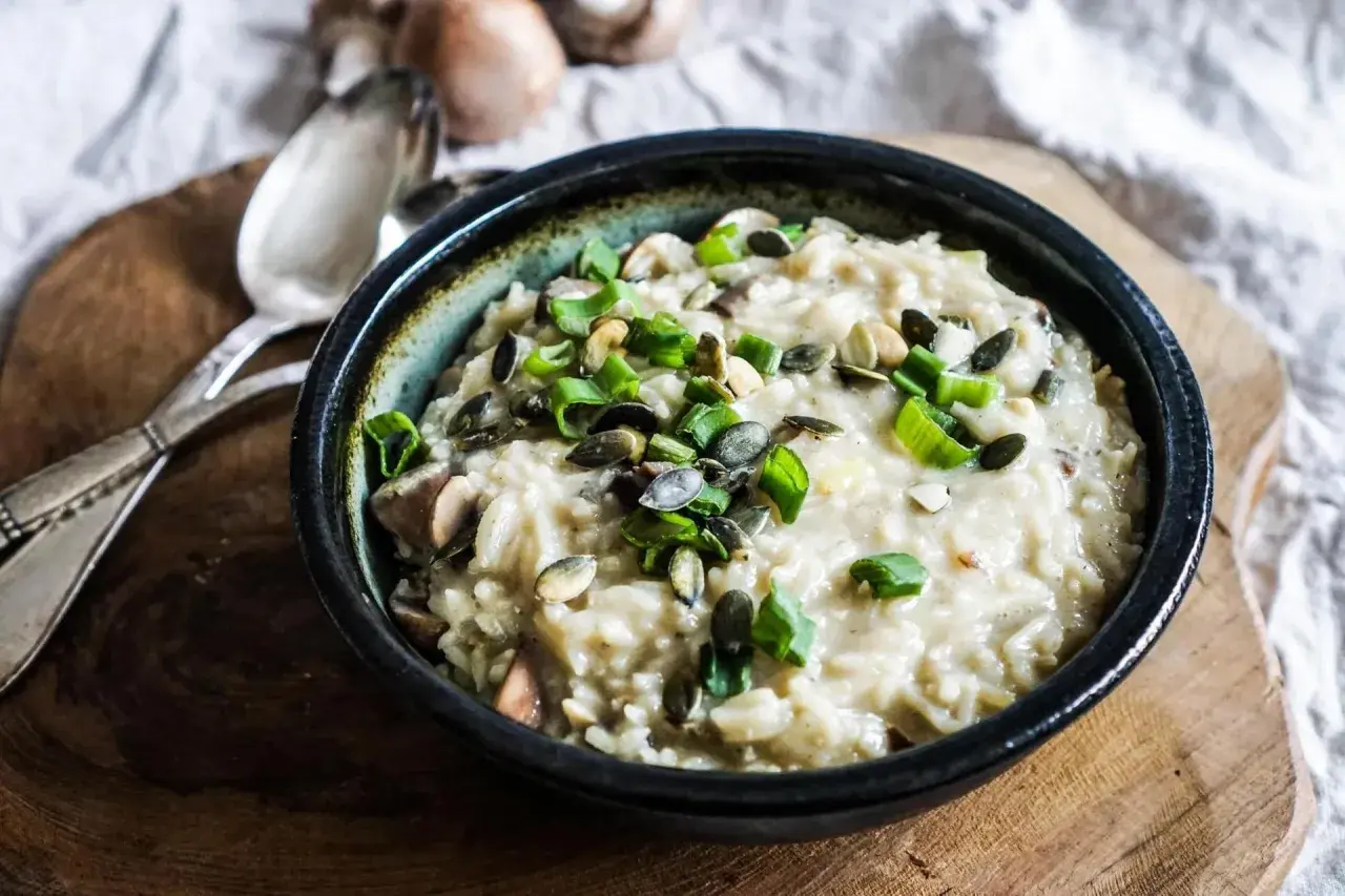 Aksamitne risotto z pieczarkami, posypane pestkami dyni i szczypiorkiem, czeka na talerzu.