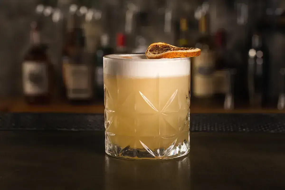 Klasyczny whisky sour przepis: orzeźwiający koktajl z pianką i plasterkiem suszonej pomarańczy.