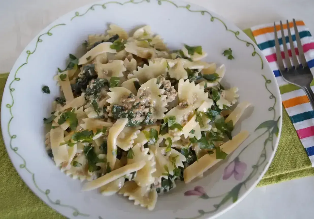 Pyszny makaron farfalle z tuńczykiem i szpinakiem, posypany świeżą natką pietruszki.