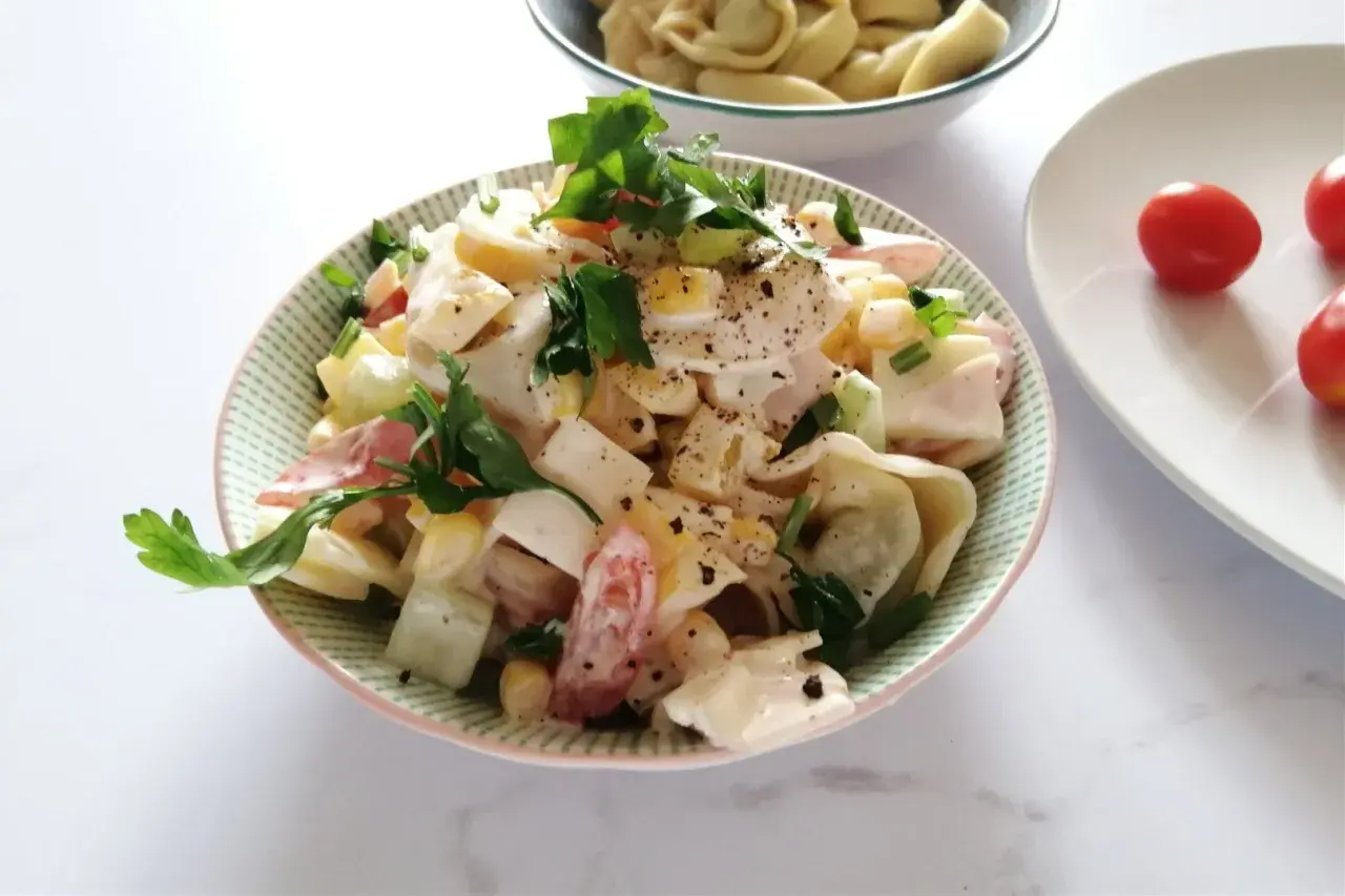 Pyszna sałatka z tortellini, jajka, kukurydzy i pomidorów, udekorowana natką pietruszki. Idealna na letnie dni, to najlepsza sałatka z tortellini.