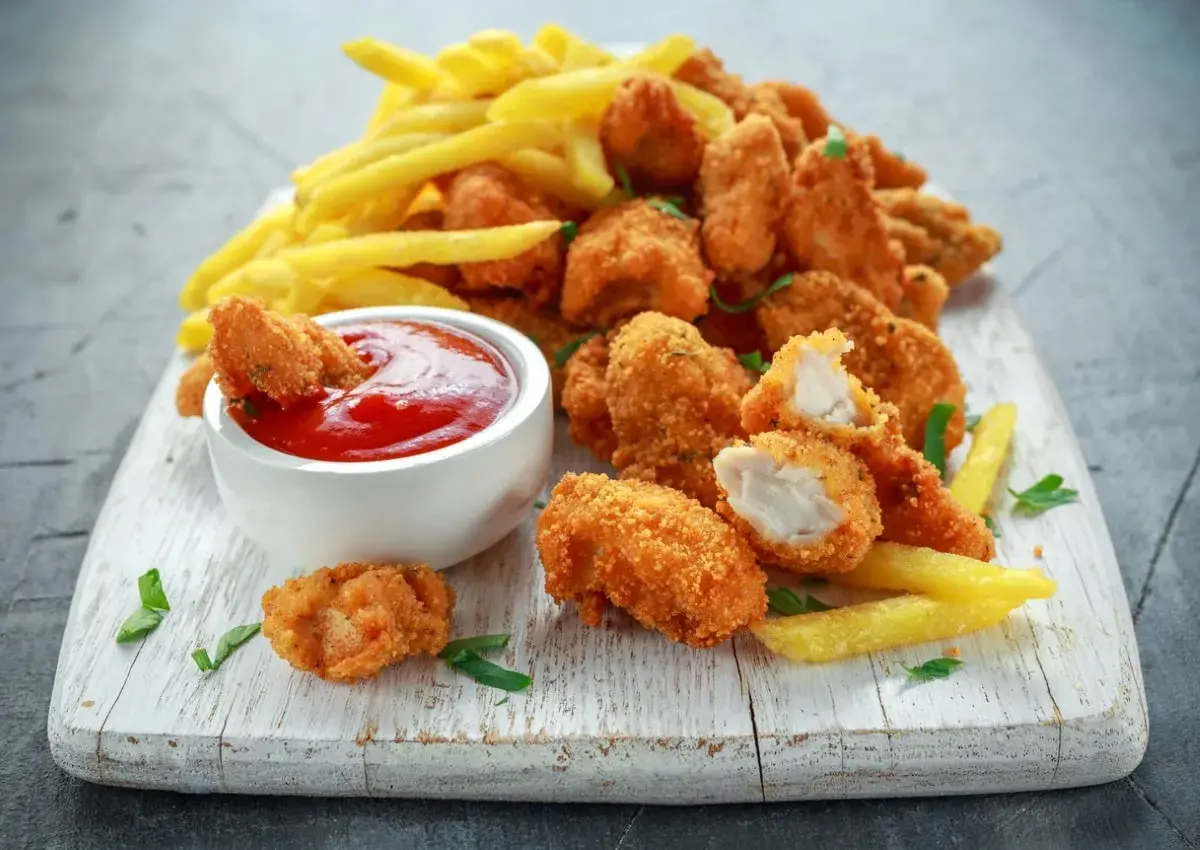 Chrupiące, złociste domowe nuggetsy jak z McDonalda, podane z frytkami i ketchupem na białej desce.