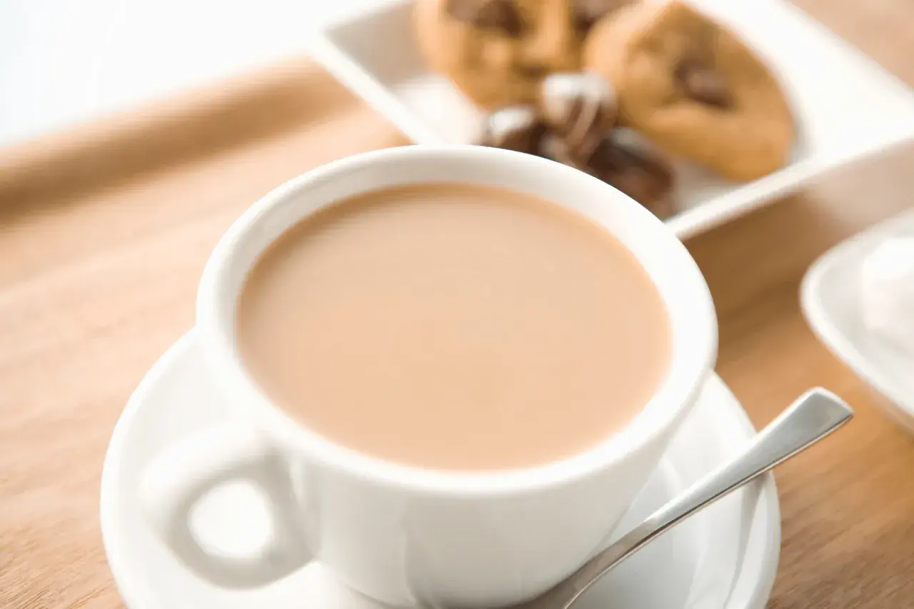 Aromaticzne cafe au lait w białej filiżance, obok ciasteczka z kawałkami czekolady. Idealny poranek.