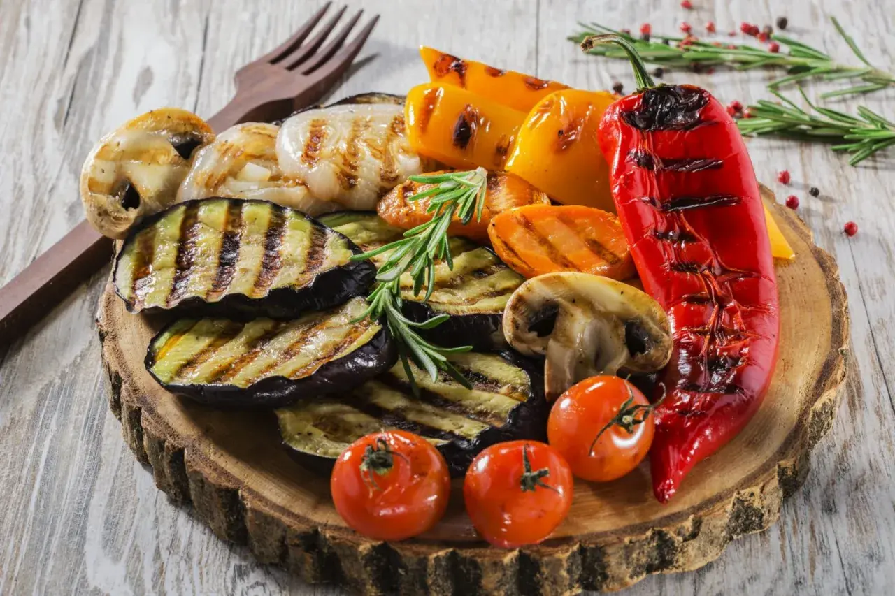 Co przygotować na grilla ze znajomymi? Grillowane bakłażany, papryki, pieczarki, pomidorki i marchewka na drewnianej desce.