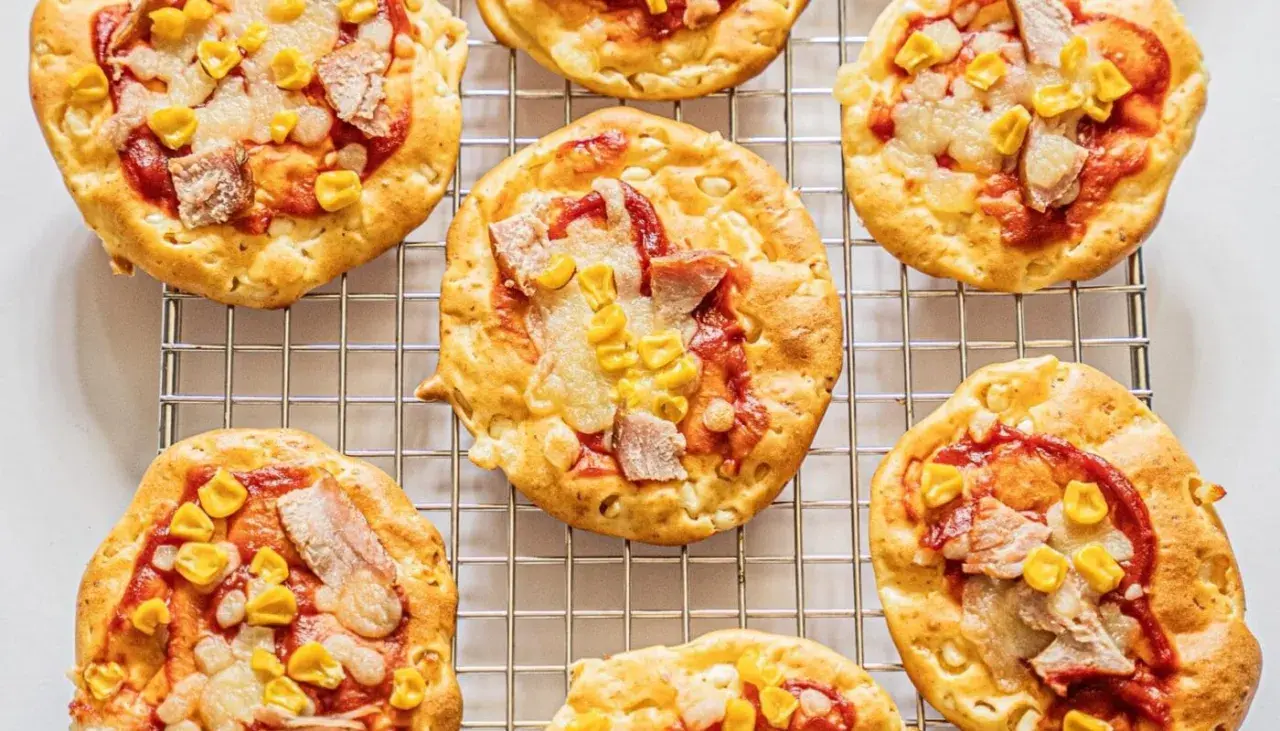 Mini pizze z serka wiejskiego, z kukurydzą i kawałkami mięsa, ułożone na metalowej kratce.
