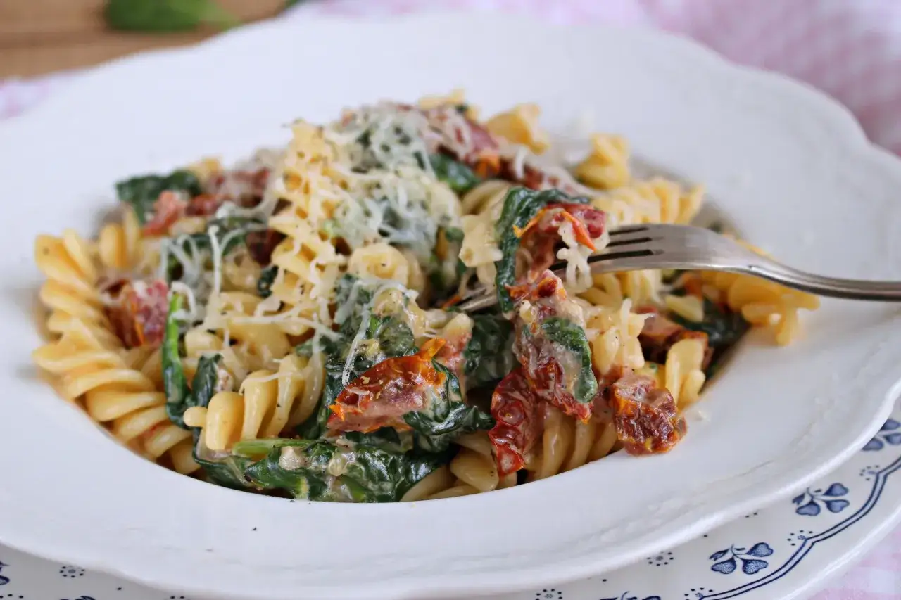 Pyszny makaron fusilli z szpinakiem, suszonymi pomidorami i kremowym sosem mascarpone, posypany parmezanem.