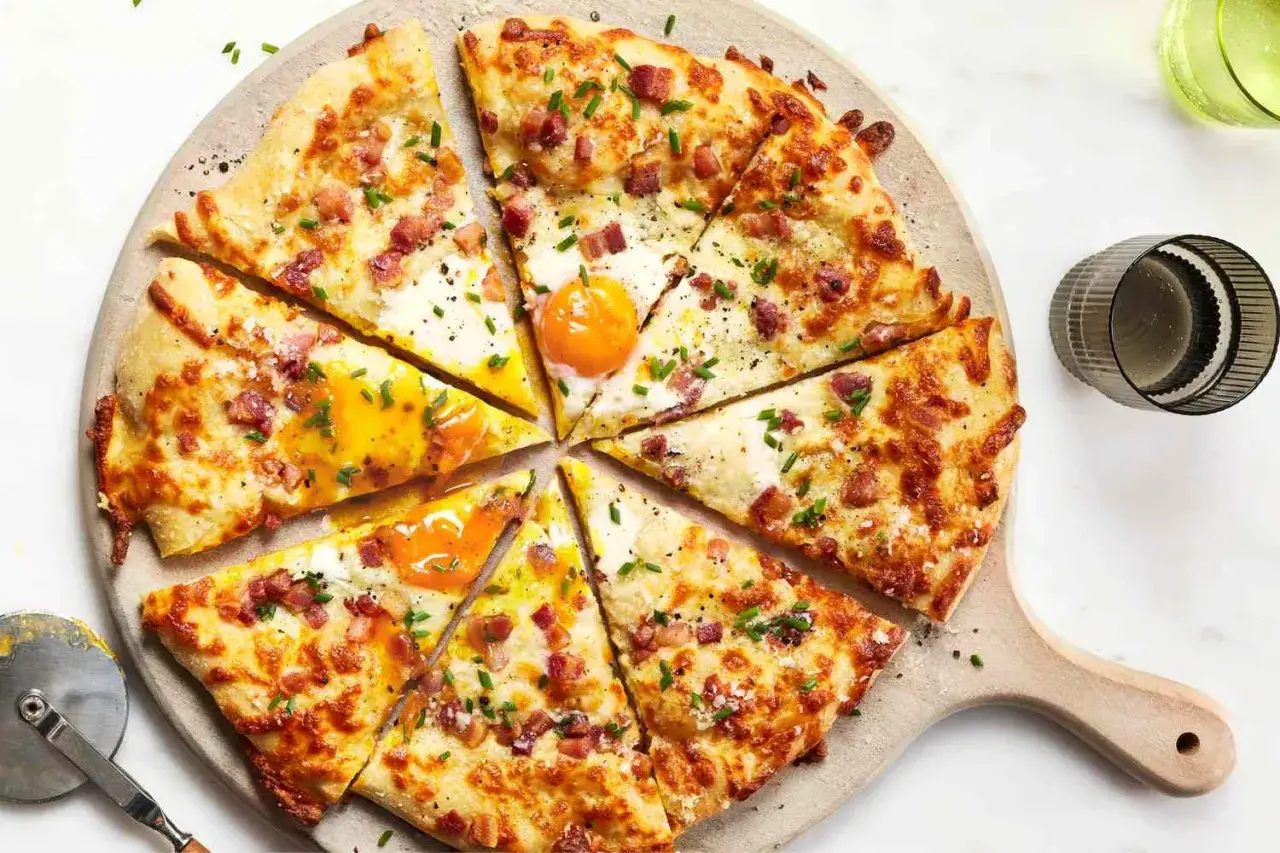Kawałki pizzy carbonara z jajkiem sadzonym, boczkiem i szczypiorkiem na drewnianej desce.